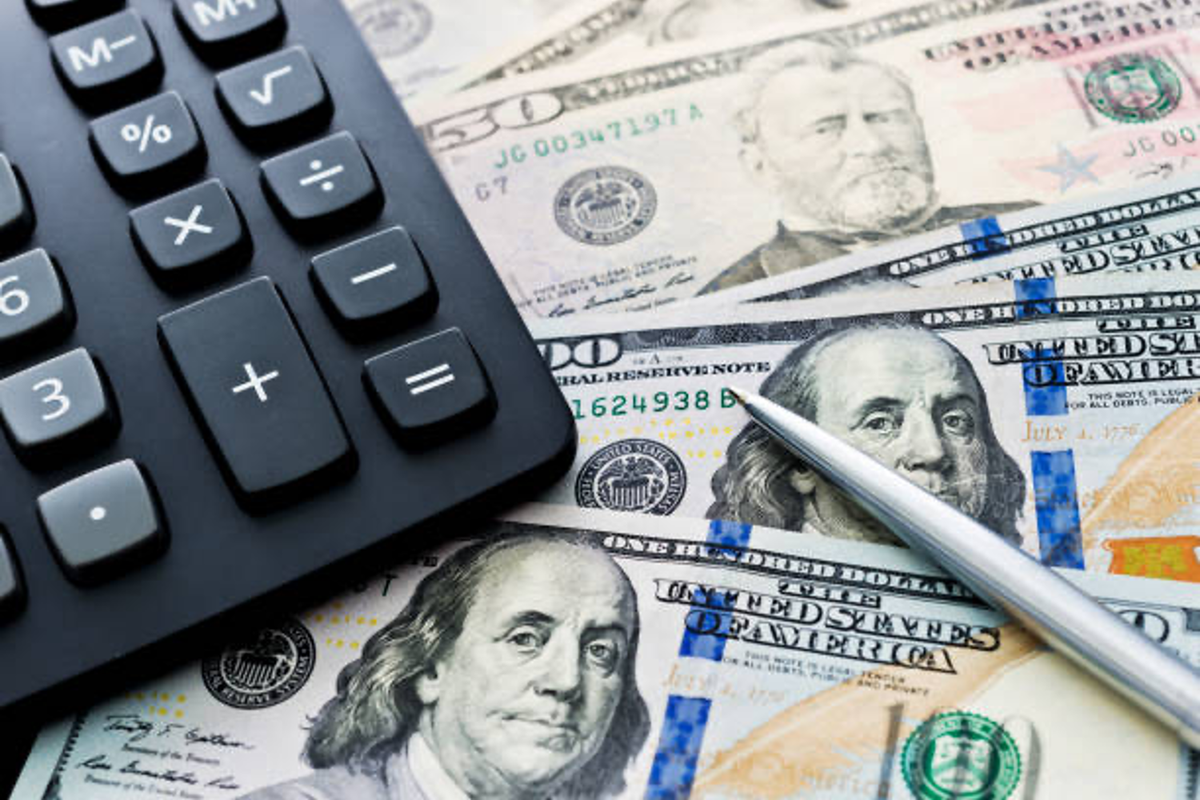 Calculator and pen on scattered US dollar bills.