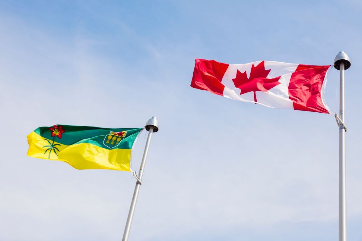Canadian and Saskatchewan flags waving under a clear blue sky.