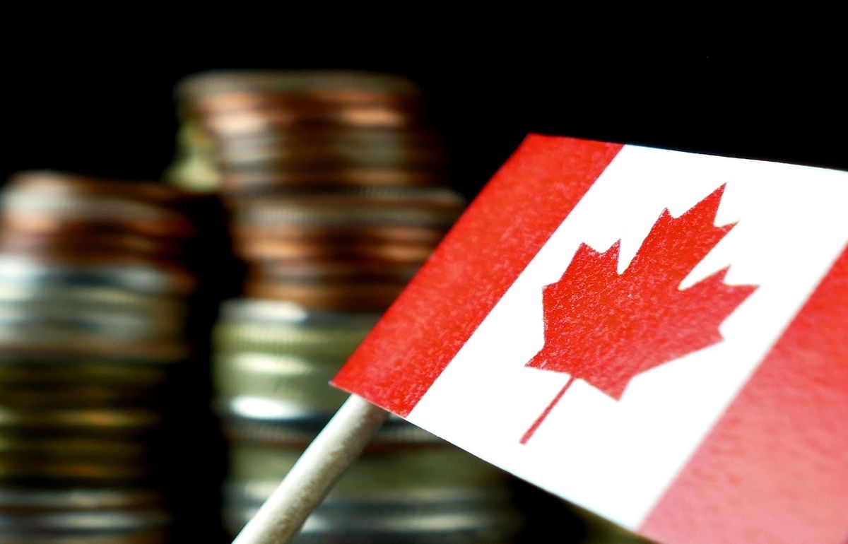Canadian flag in front of stacked coins, black background.