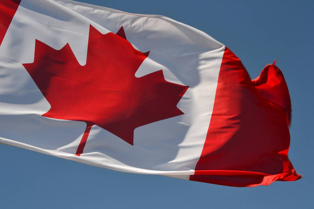 Canadian flag waving against clear blue sky.