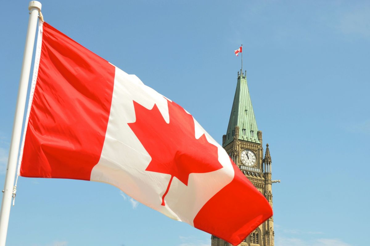 Canadian flag waving near a clock tower with clear blue sky.
