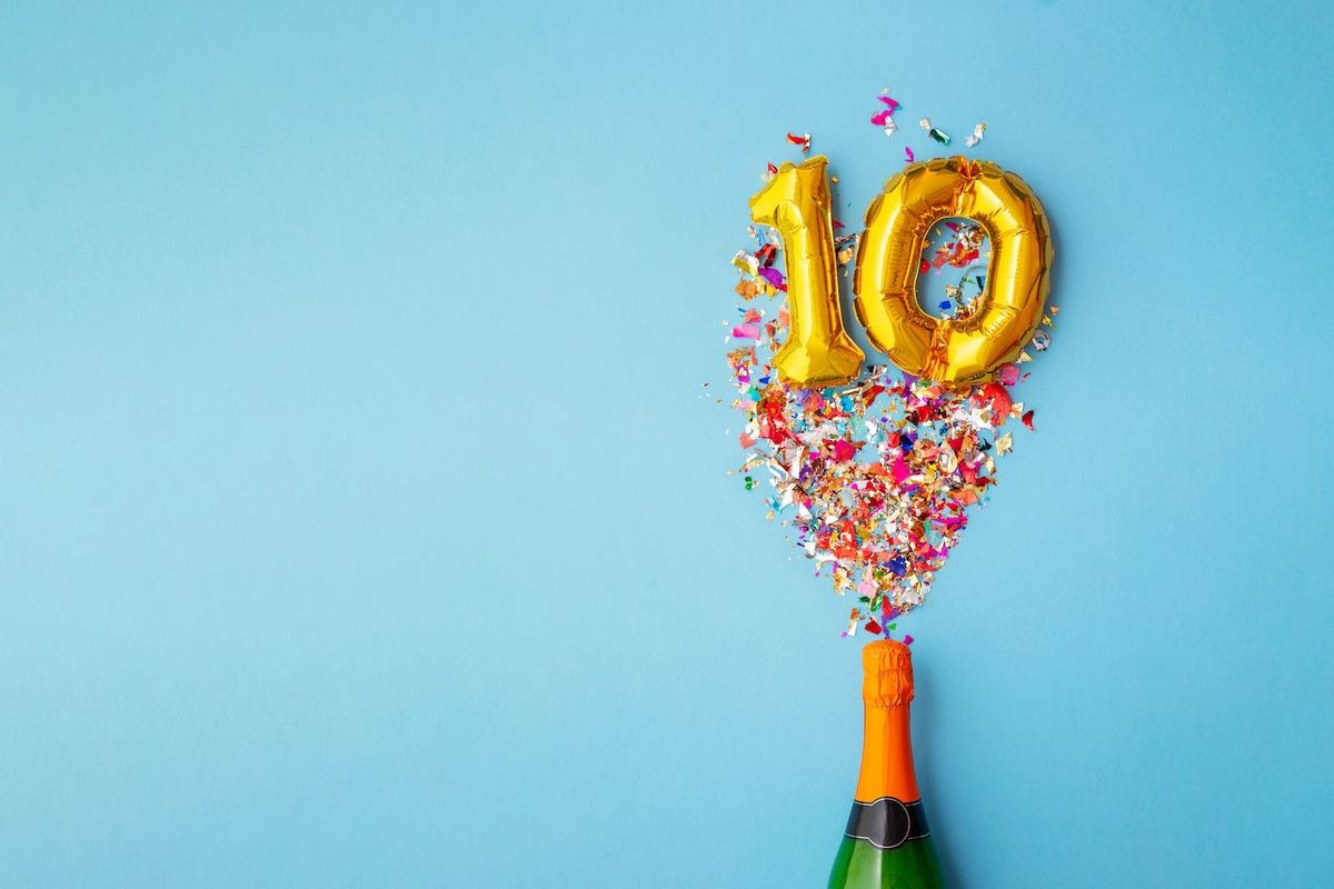 Champagne bottle with confetti and gold "10" balloons on blue background.