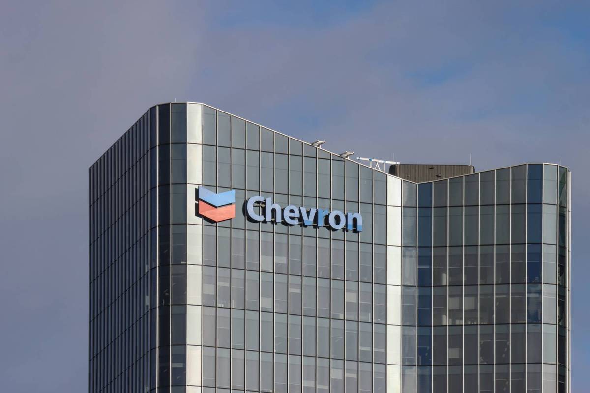 Chevron logo on glass skyscraper under cloudy sky.
