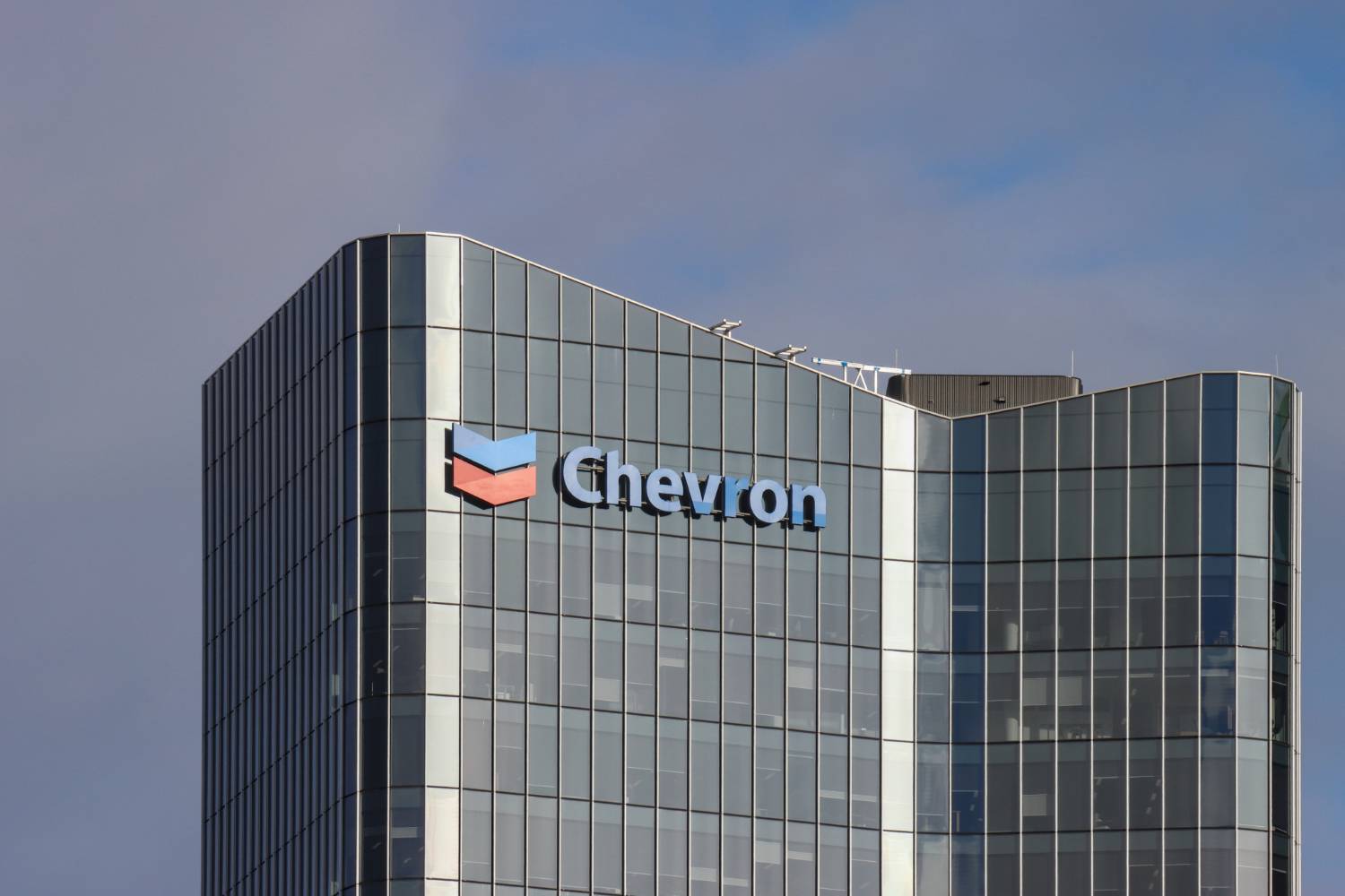 Chevron logo on glass skyscraper under cloudy sky.