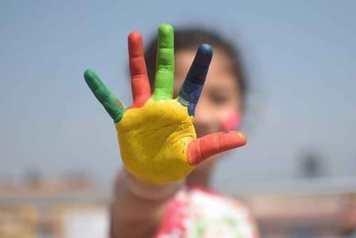 child's outstretched hand holding up five fingers with multicolored finger paints
