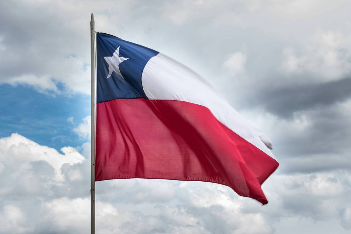 Chilean flag waves against a cloudy blue sky with a metallic pole.