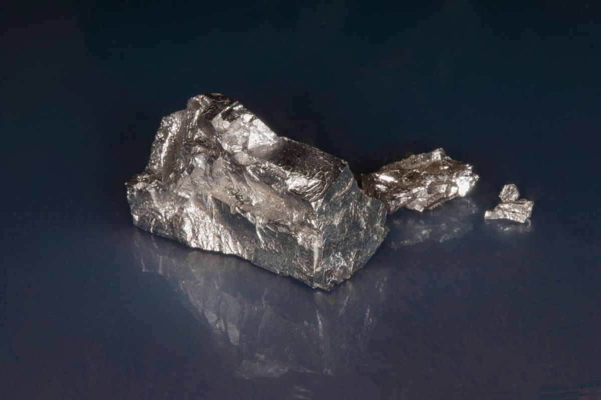 Chromium ore sitting on shiny surface with visible reflection.