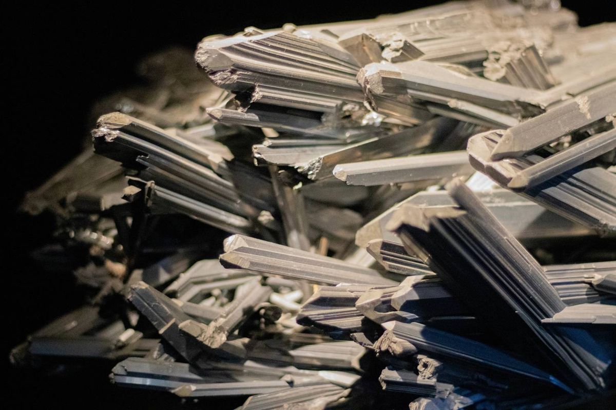 Close-up of antimony mineral Stibnite, made up of jagged, metallic crystal formations with sharp edges against a dark, blurred background.