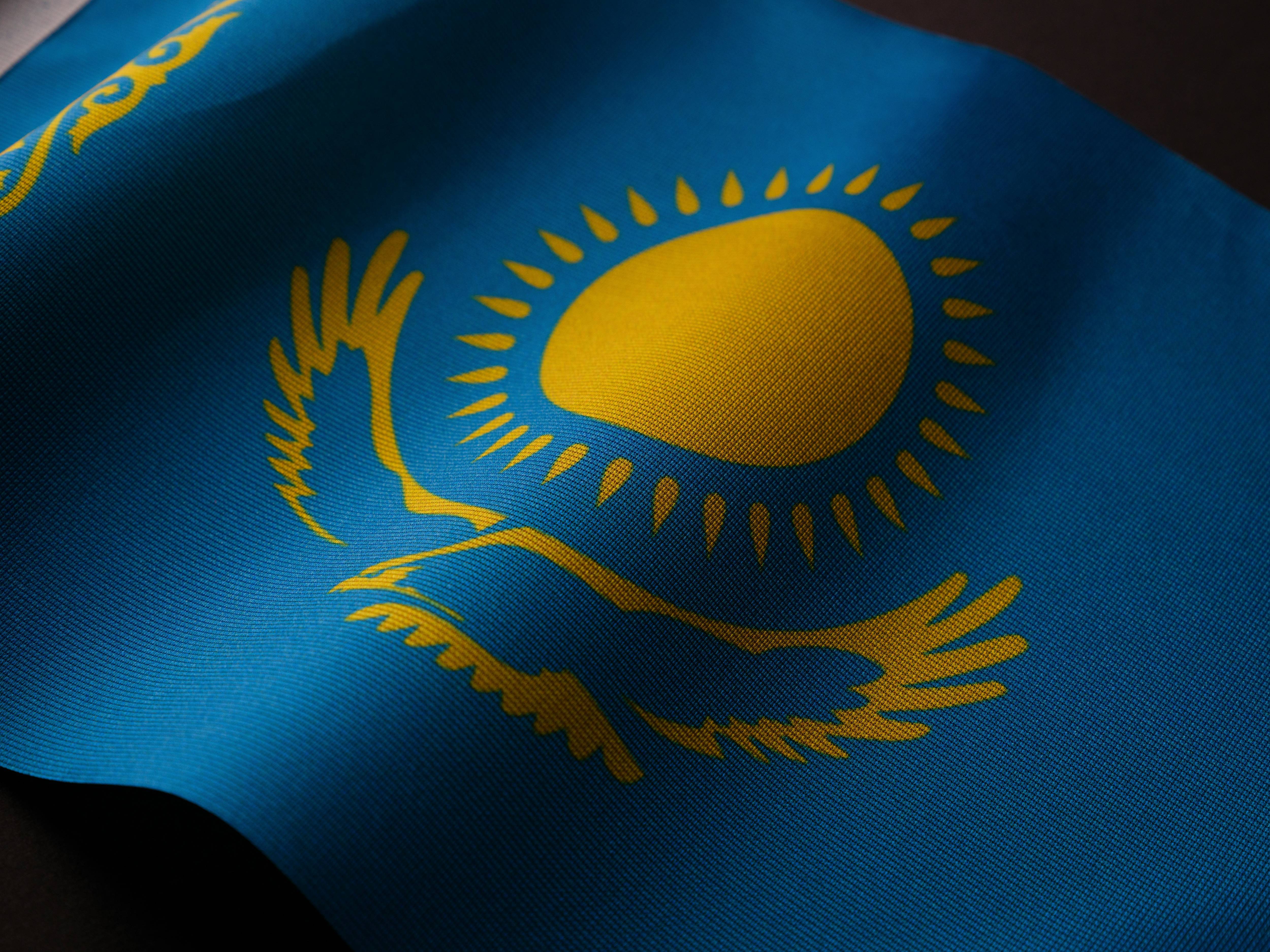 Close-up of Kazakhstan flag with sun and eagle design on blue fabric.