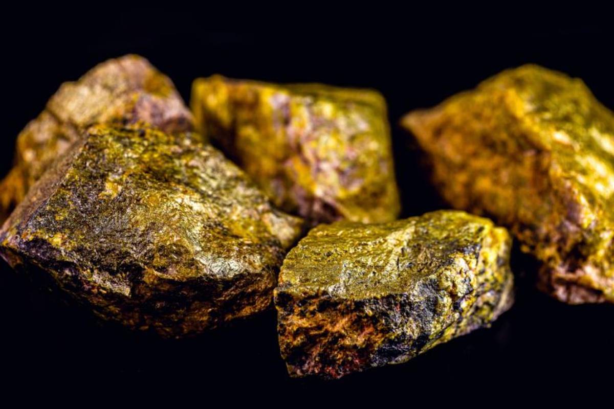 Close up of pieces of yellow uranium rock on a black surface.