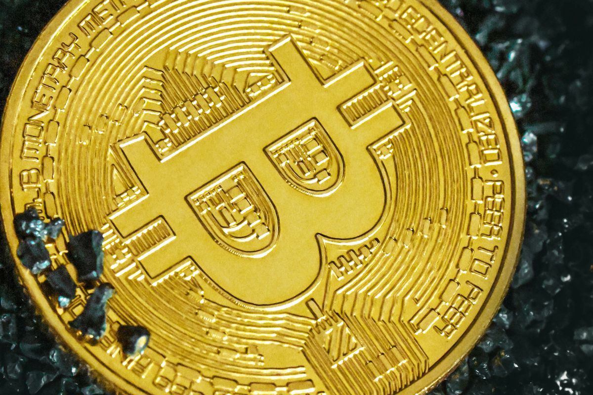 Closeup of a gold Bitcoin with intricate details on a dark, textured surface.