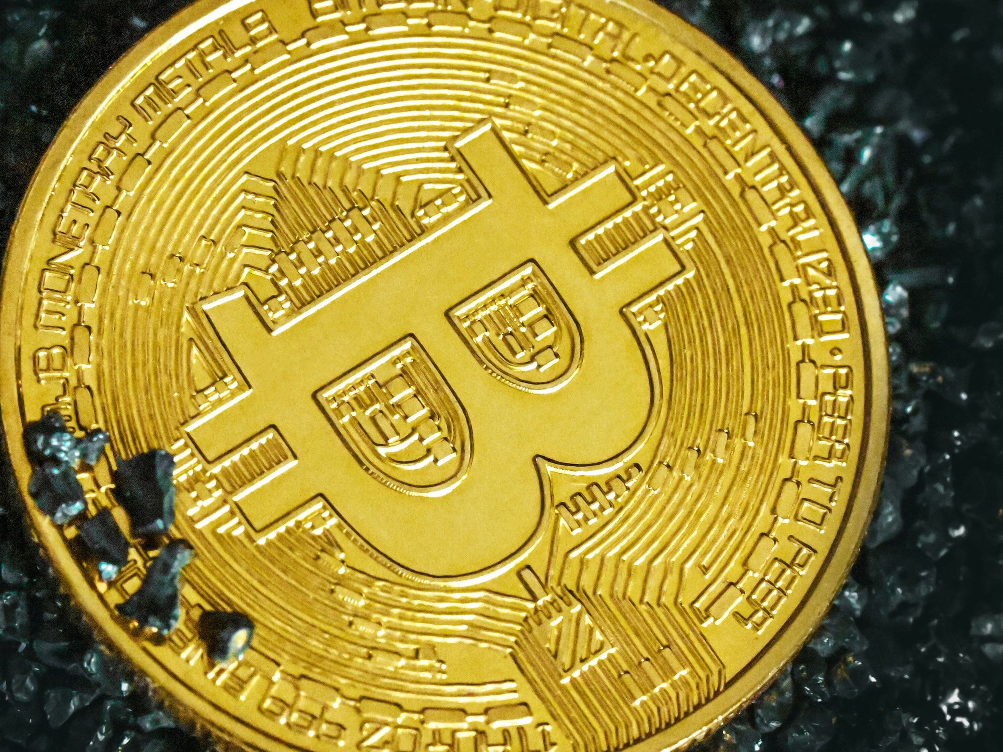 Closeup of a gold Bitcoin with intricate details on a dark, textured surface.