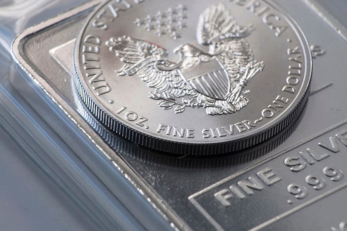 Closeup of a silver coin on a silver bullion bar with embossed text.