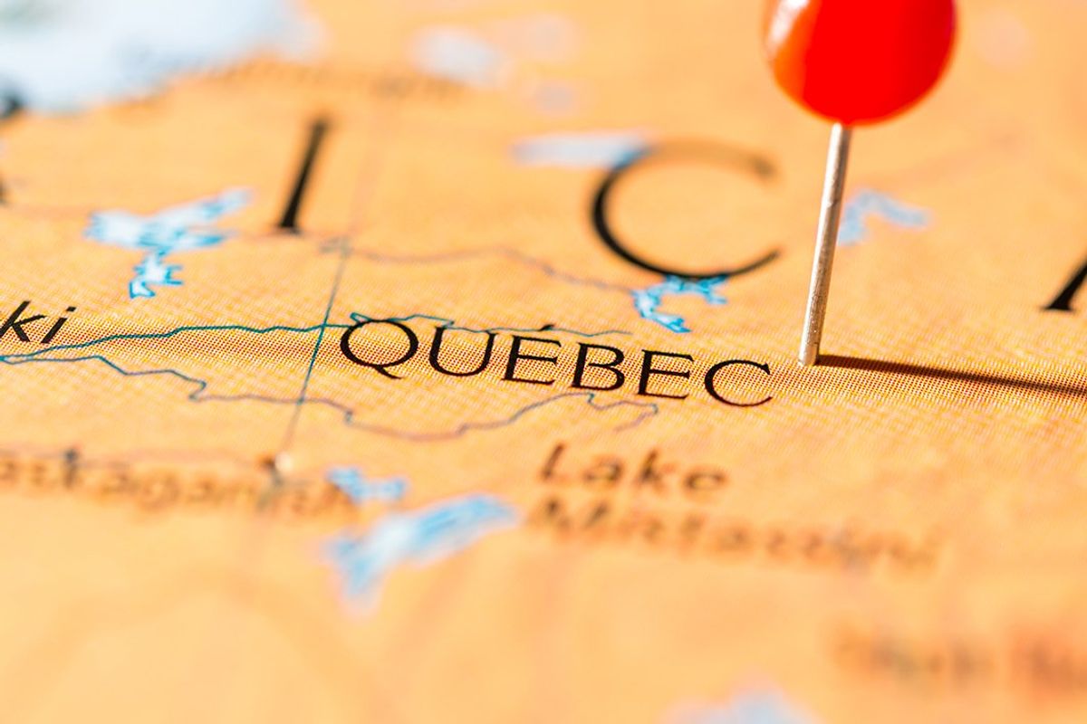 closeup of paper map with a pin next to the word quebec