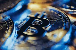 Closeup of shiny gold Bitcoin coins illuminated with blue and yellow light.