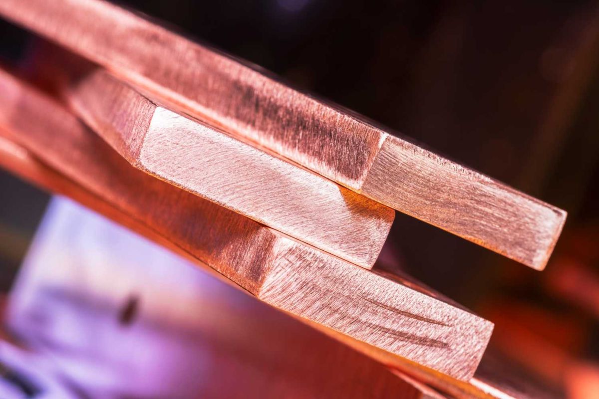 Closeup of stacked, polished copper bars with a soft purple and orange background.