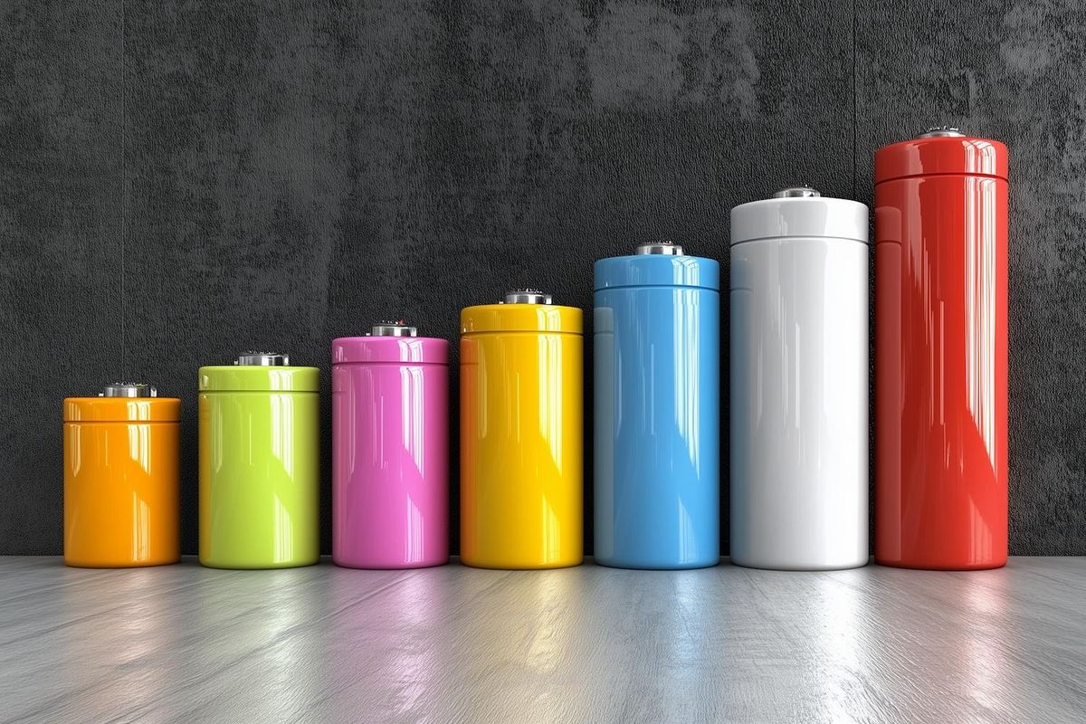 Colorful batteries arranged by size against a dark textured wall.