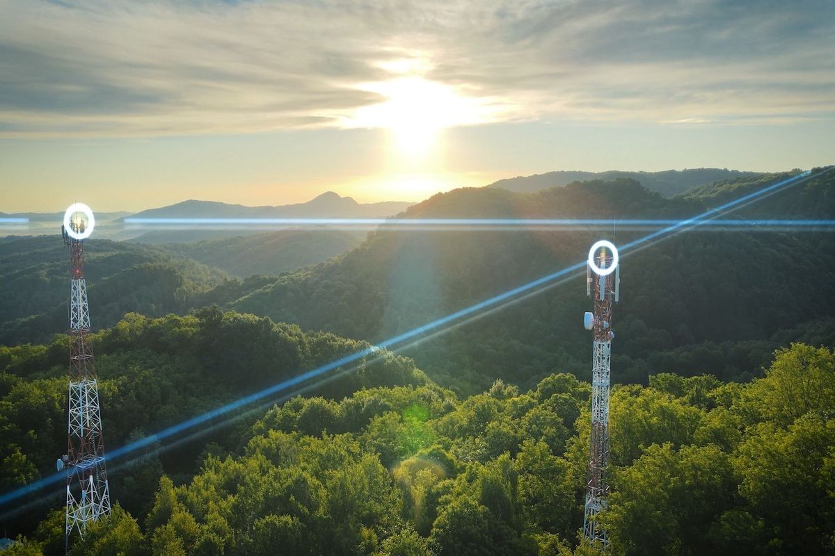 Communication towers amid green hills at sunrise with blue transmission lines connecting them.