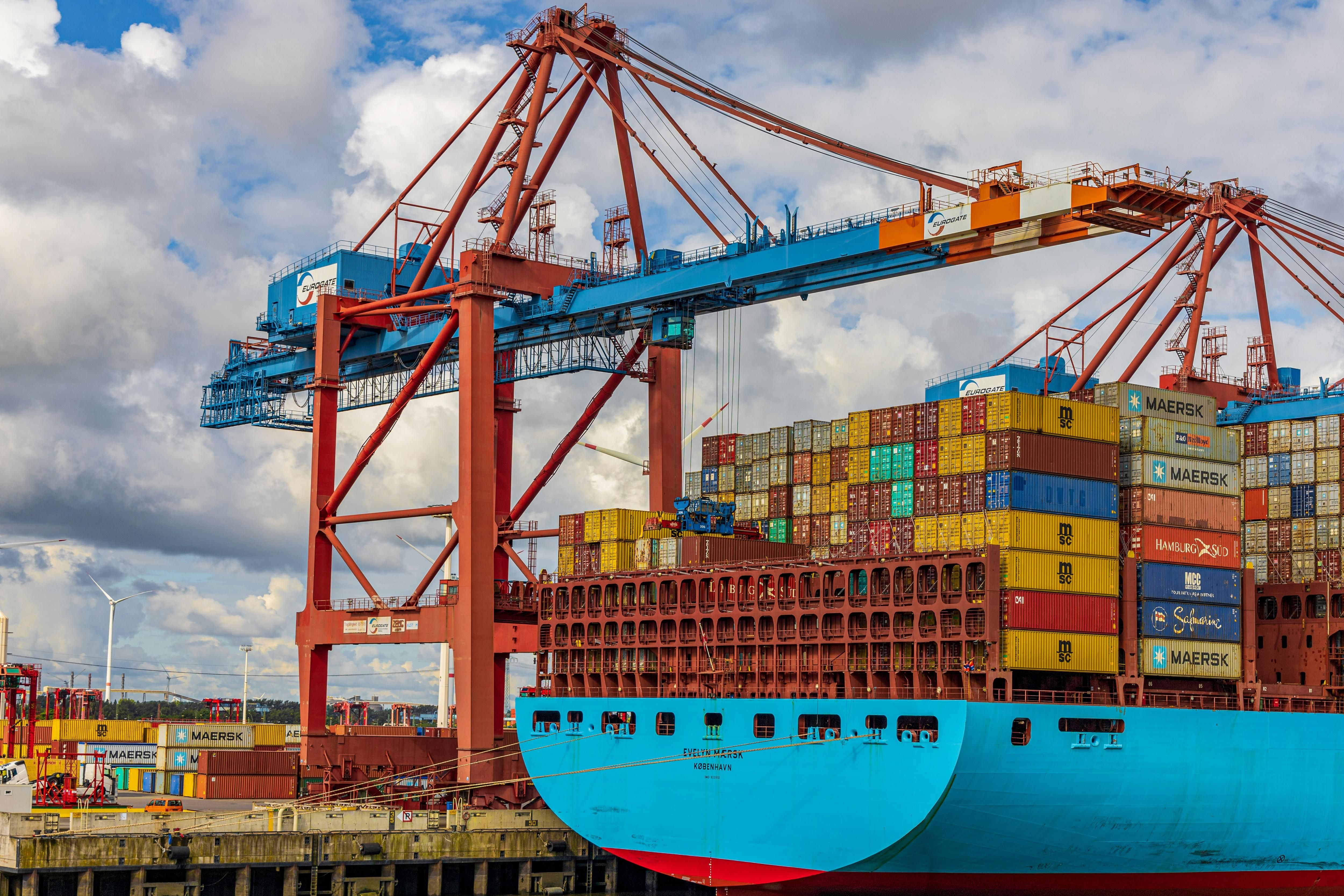 Container ship docked at port with cranes and stacked cargo containers.
