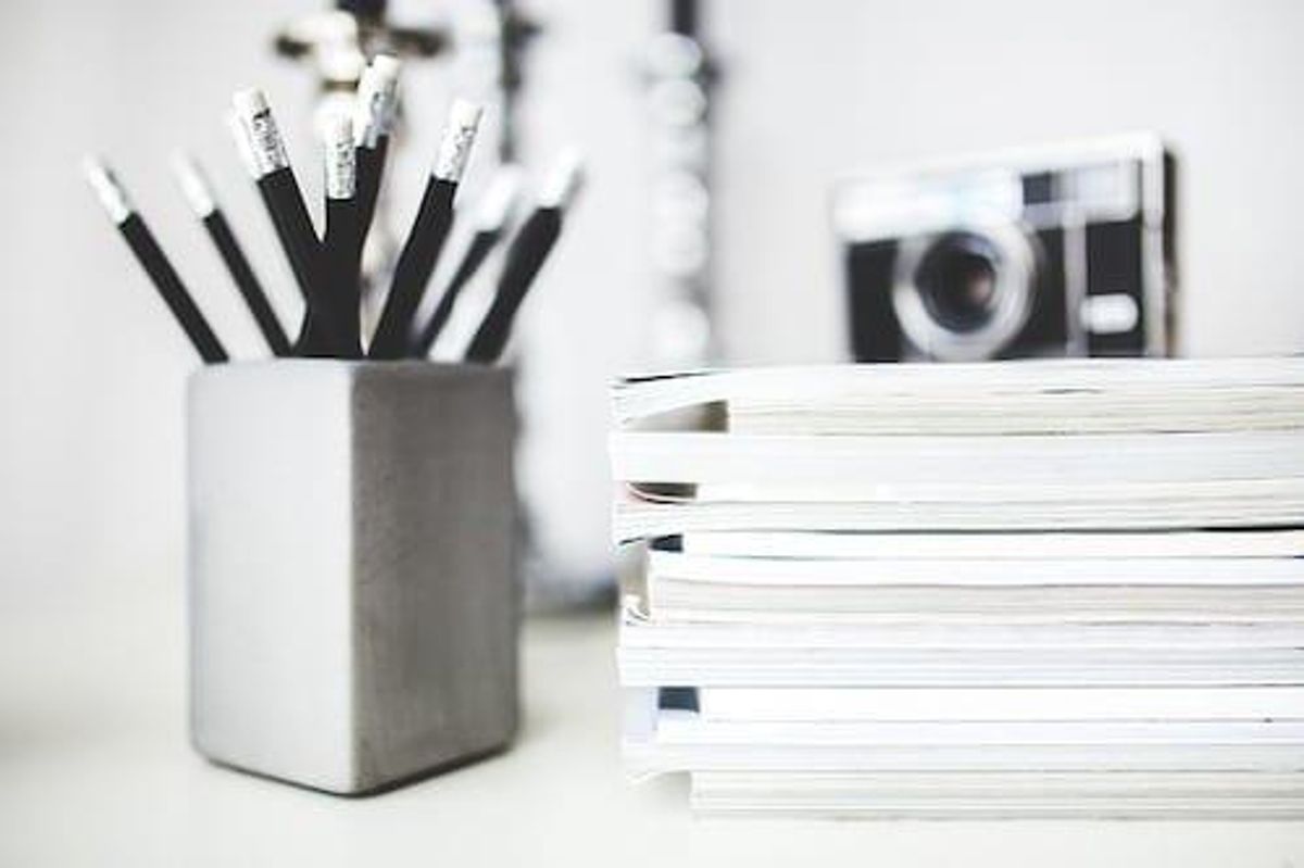 container with pencils, stack of notebooks and camera on a desk