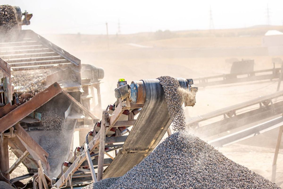 Conveyor belt depositing gravel at an open-pit mine under a clear sky.