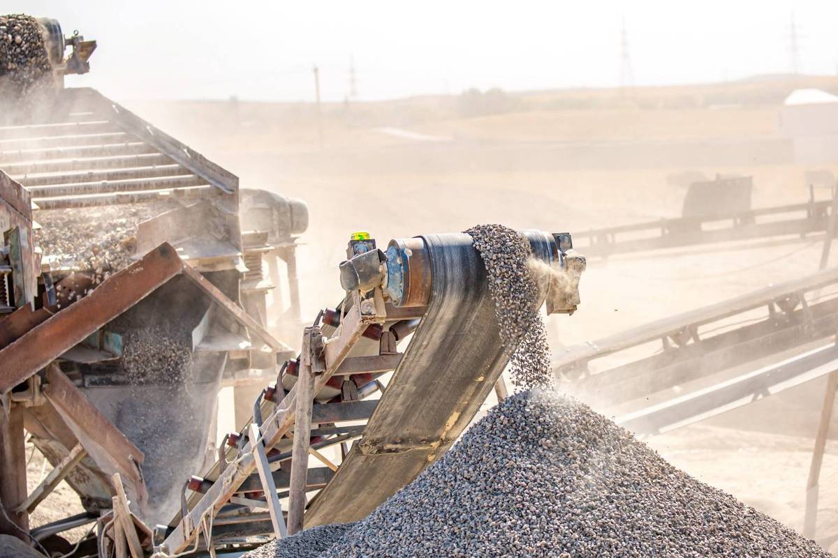 Conveyor belt depositing gravel at an open-pit mine under a clear sky.