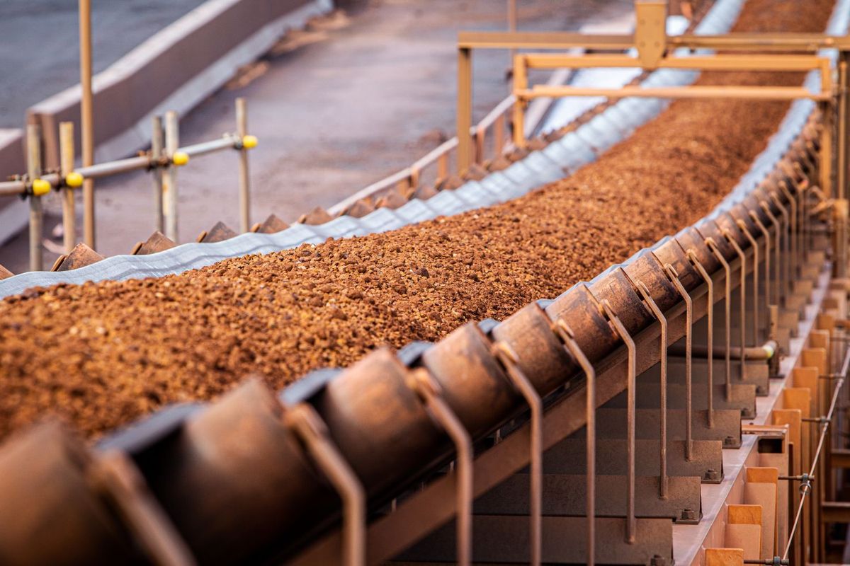 Conveyor belt transporting brown mineral ore in a mining industrial setting.