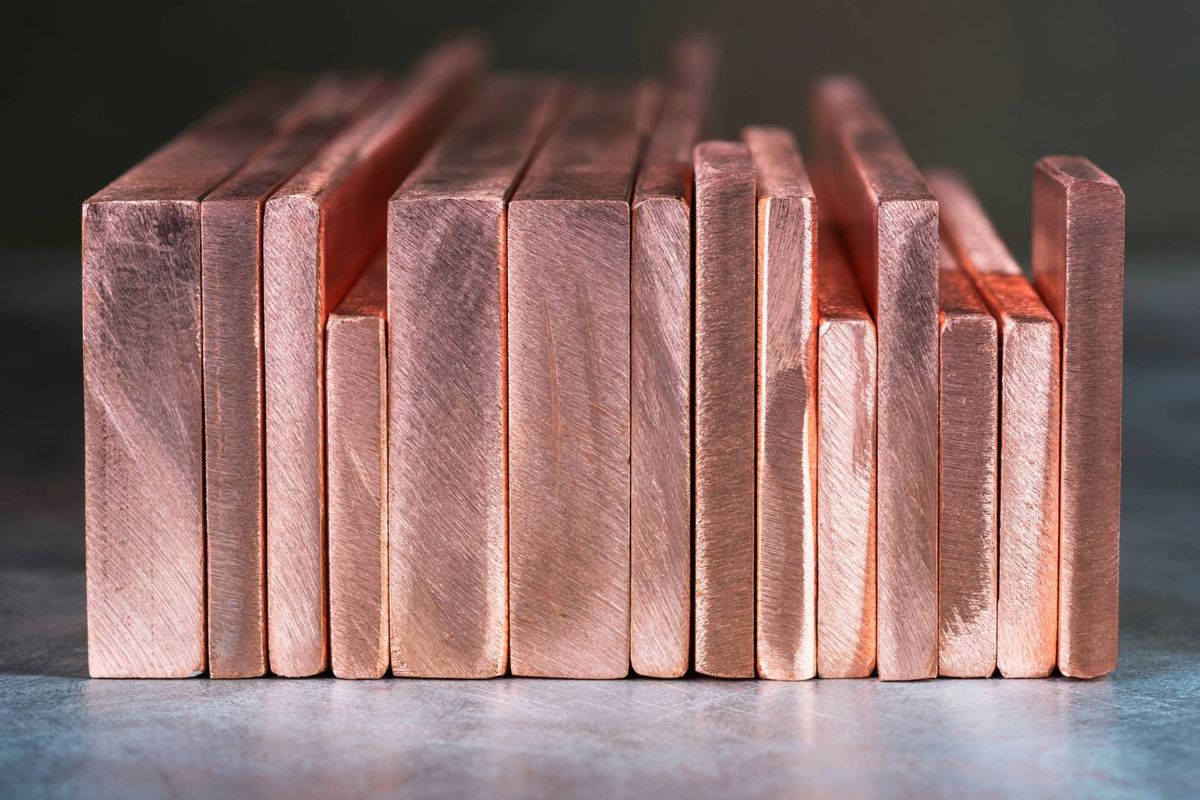 Copper bars of varying thickness neatly stacked on reflective gray surface.