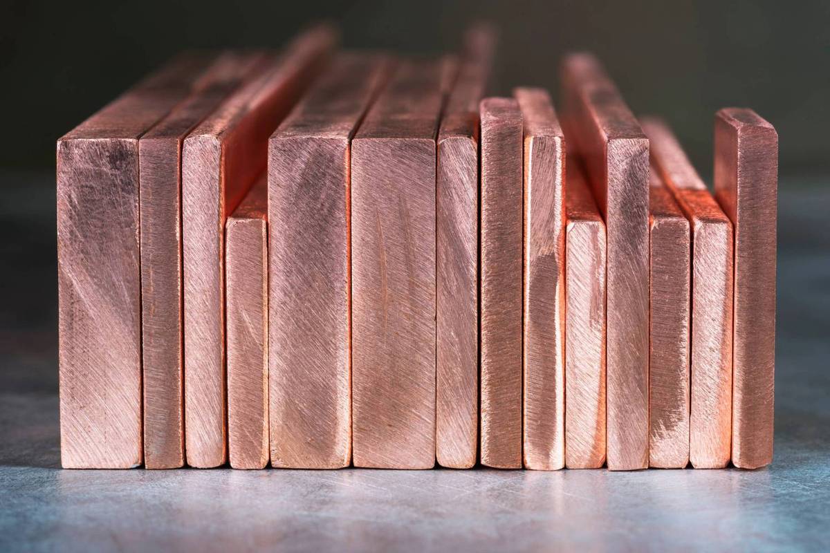 Copper bars of varying thickness neatly stacked on reflective gray surface.