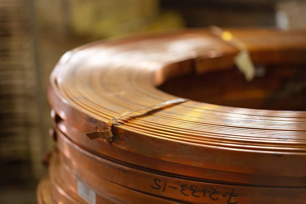 Copper coil stack with numbers written on it, in front of a blurred industrial background.