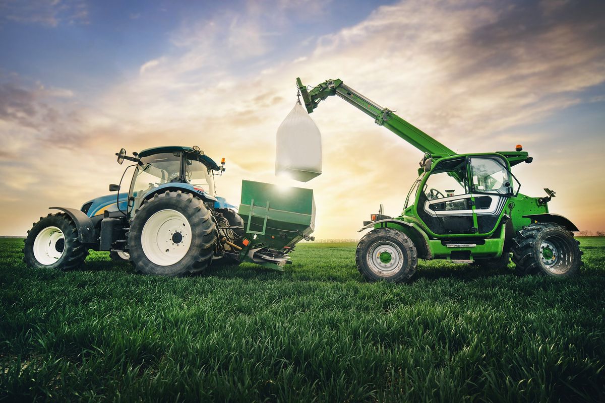Crane puts a sack of fertilizer on a trailer in a field in the spring.