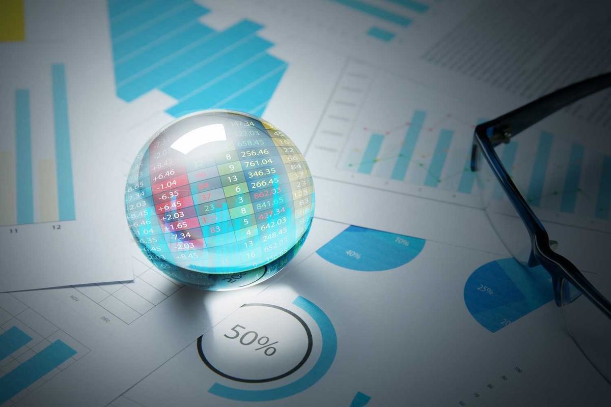 Crystal ball over financial charts and graphs, with glasses beside.