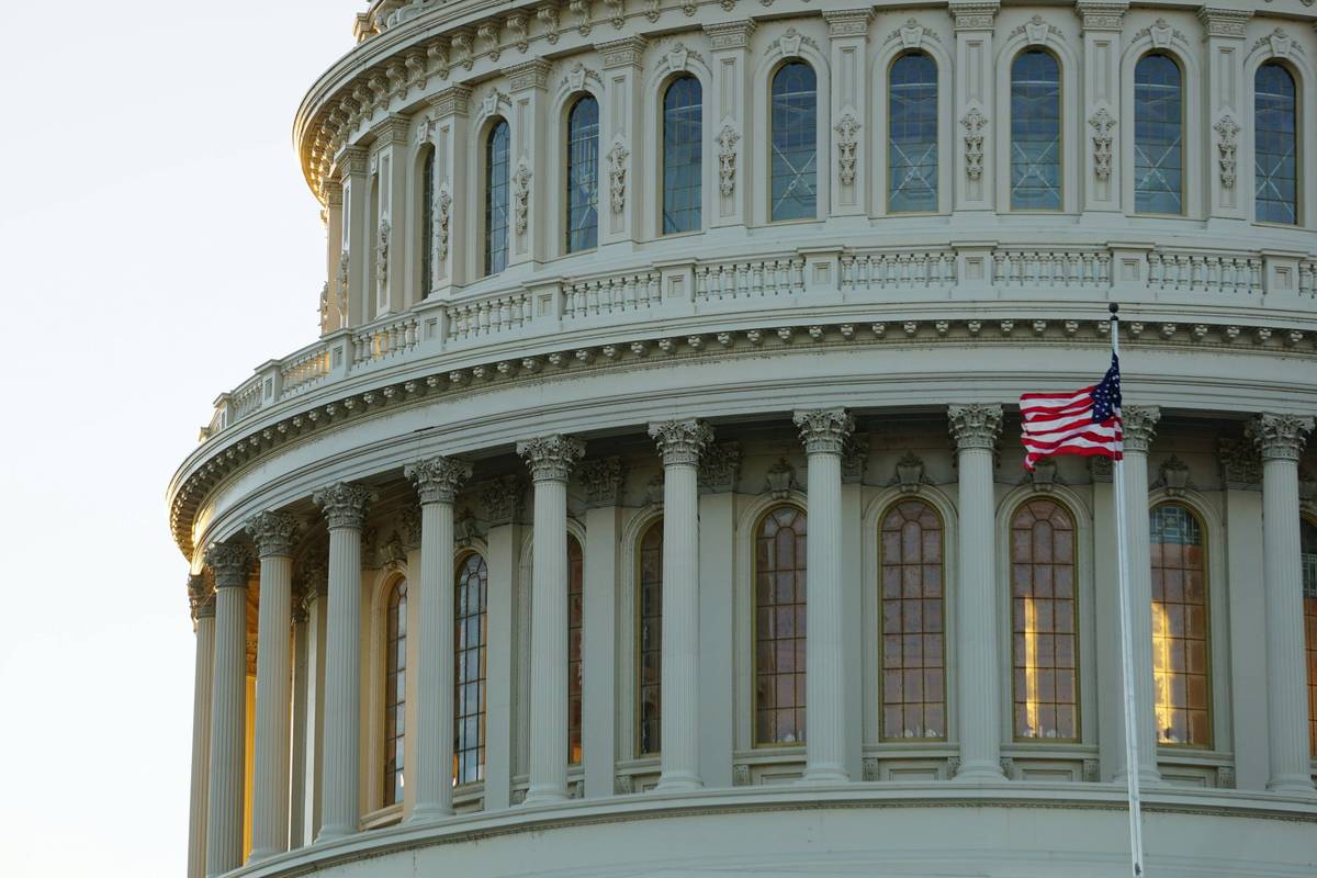 Dome of neoclassical building with arched windows and US flag flying in front.