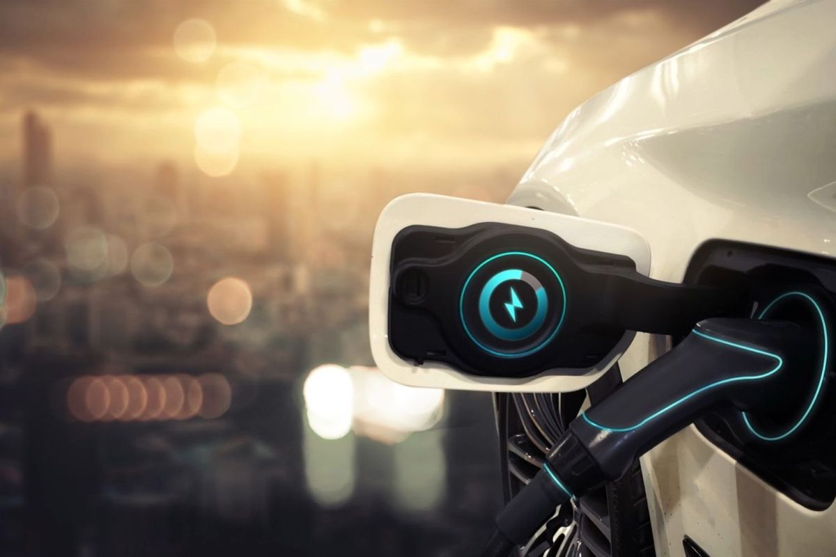 Electric car charging with cityscape at sunset in the background.