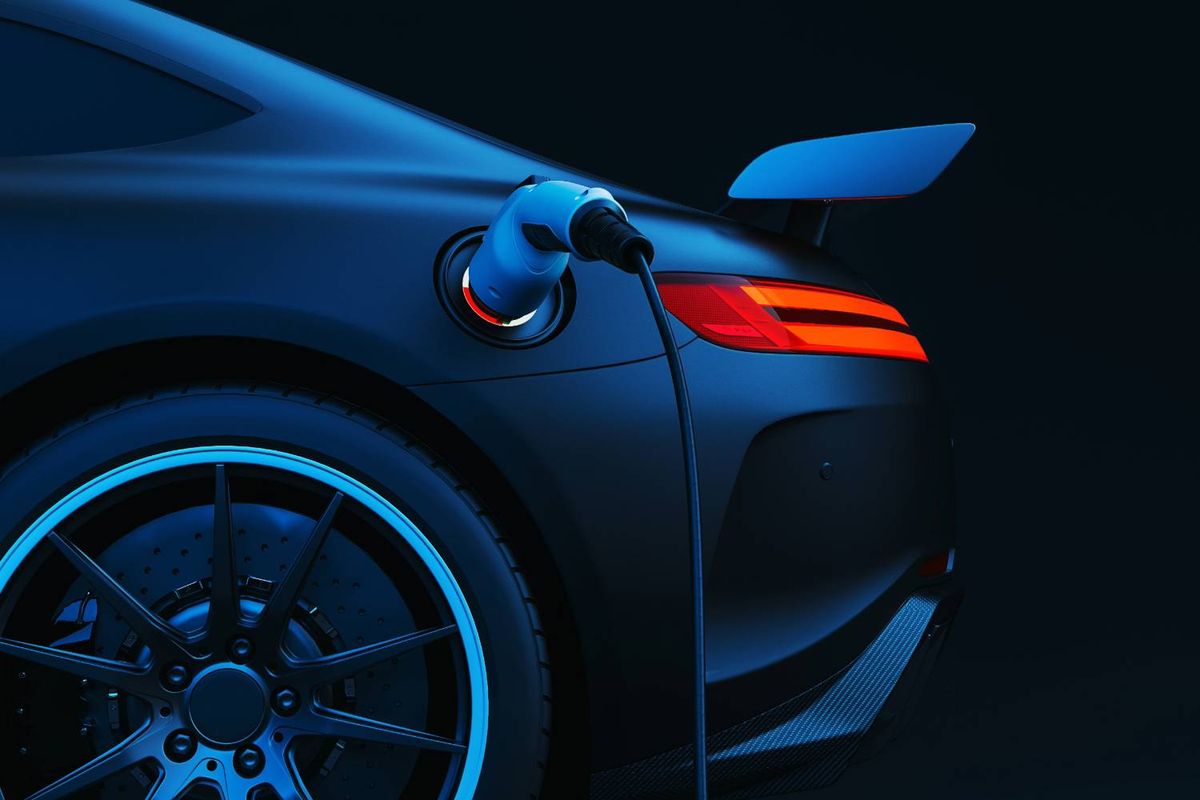 Electric sports car charging at night, rear view with taillights and charging cable.