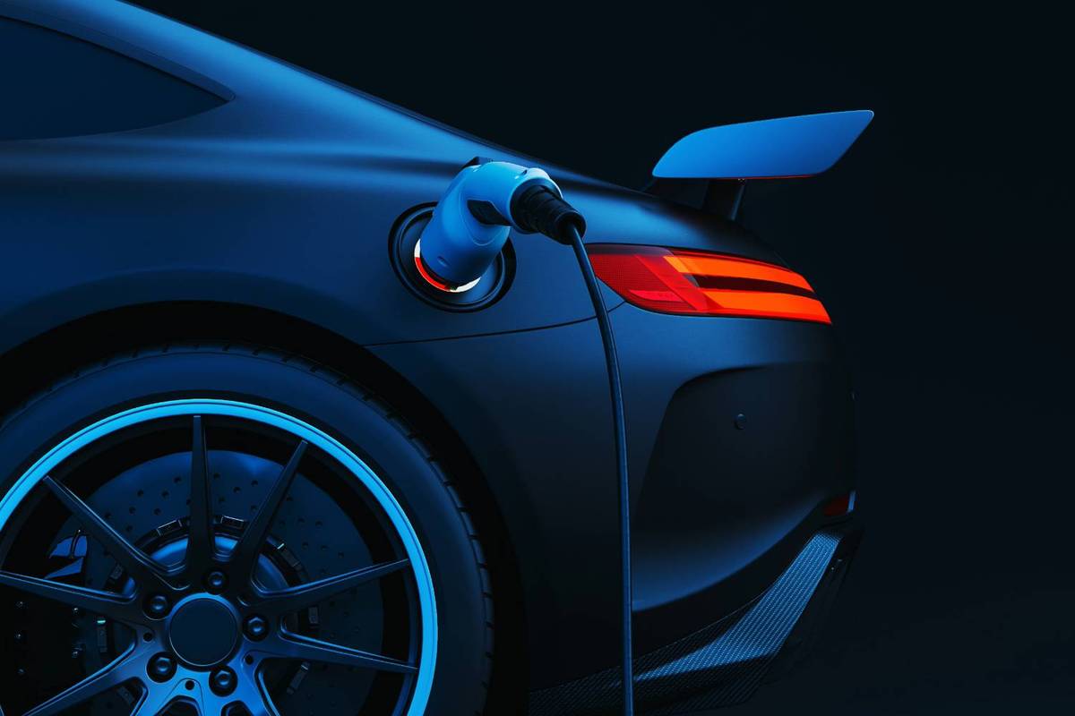 Electric sports car charging at night, rear view with taillights and charging cable.