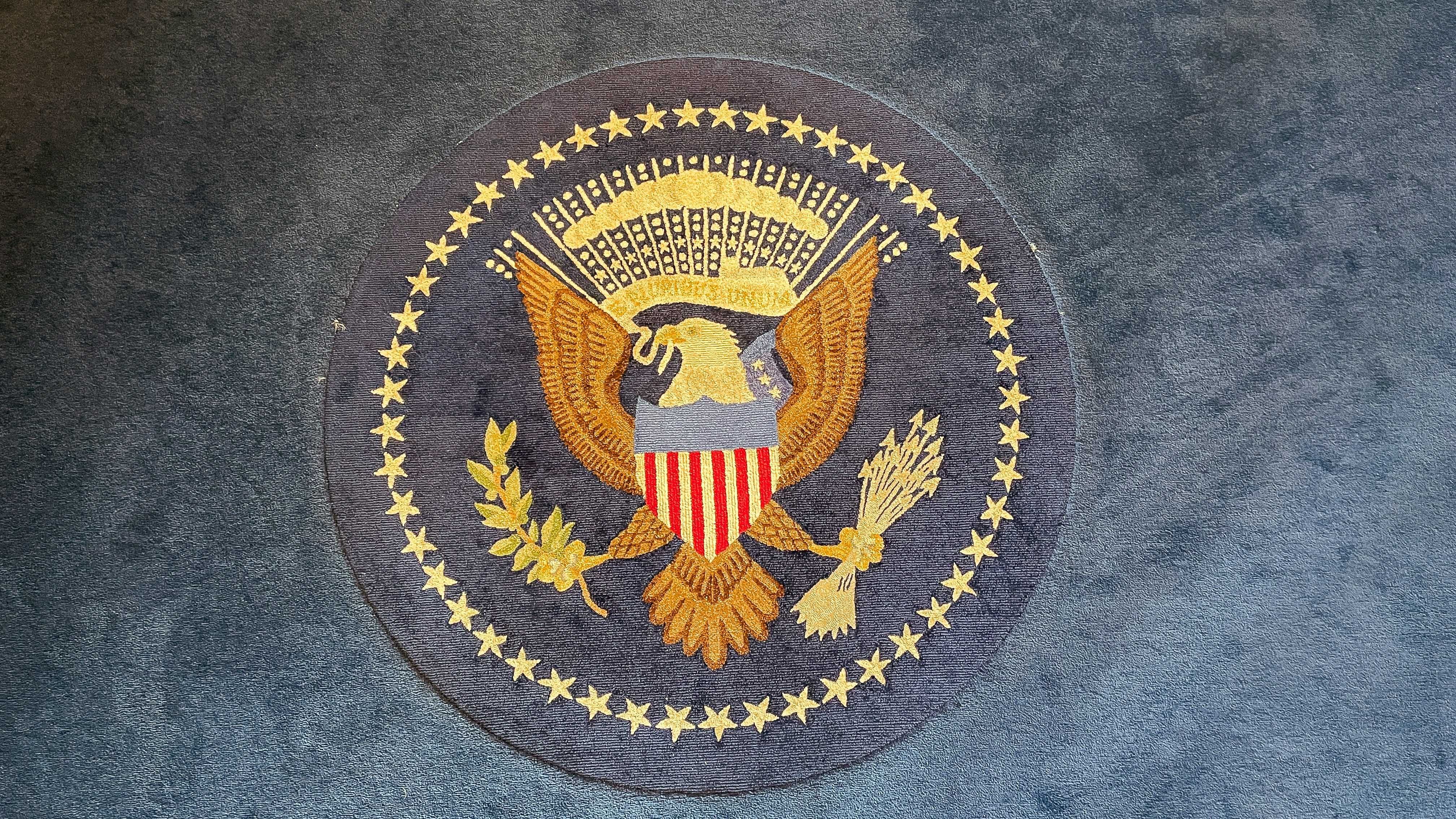 Embroidered US presidential seal with an eagle on a blue carpet.