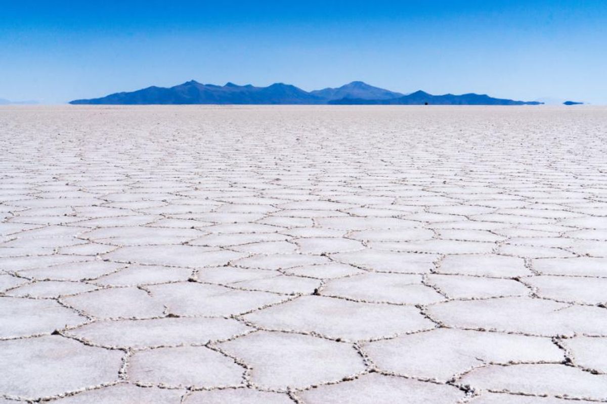 Expansive salt flat with polygonal patterns, distant mountains under a clear blue sky.