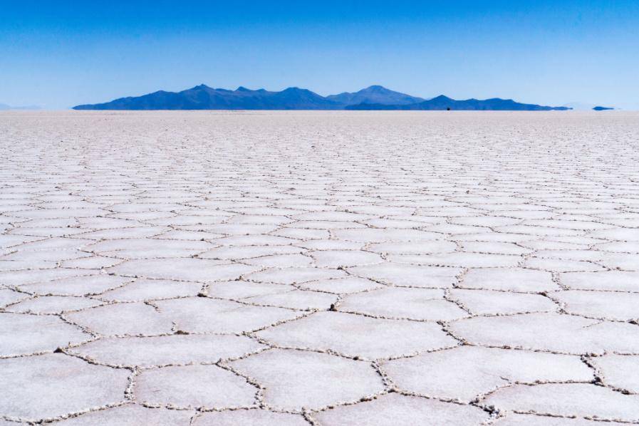 Expansive salt flat with polygonal patterns, distant mountains under a clear blue sky.