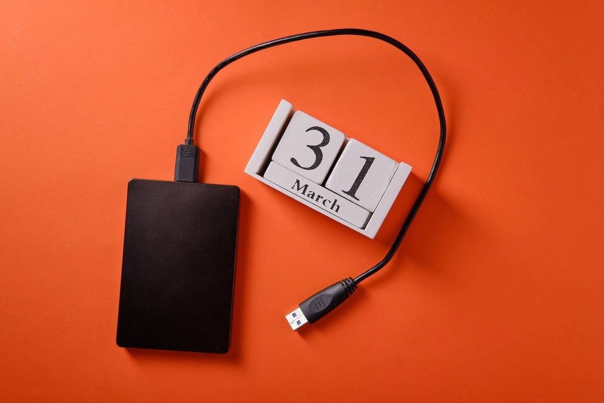External hard drive with USB cable is next to a wooden calendar displaying "31 March" on orange background.