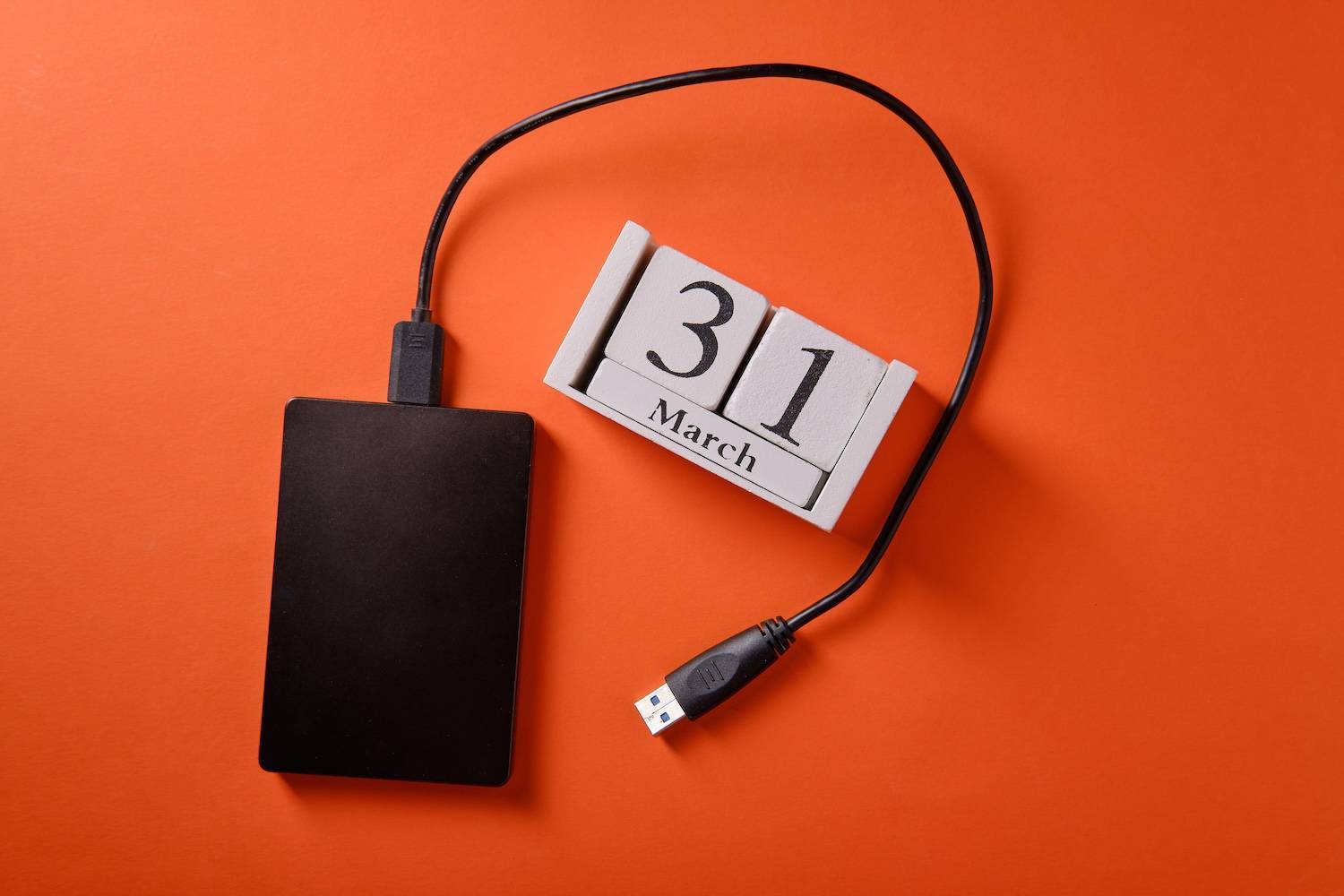 External hard drive with USB cable is next to a wooden calendar displaying "31 March" on orange background.