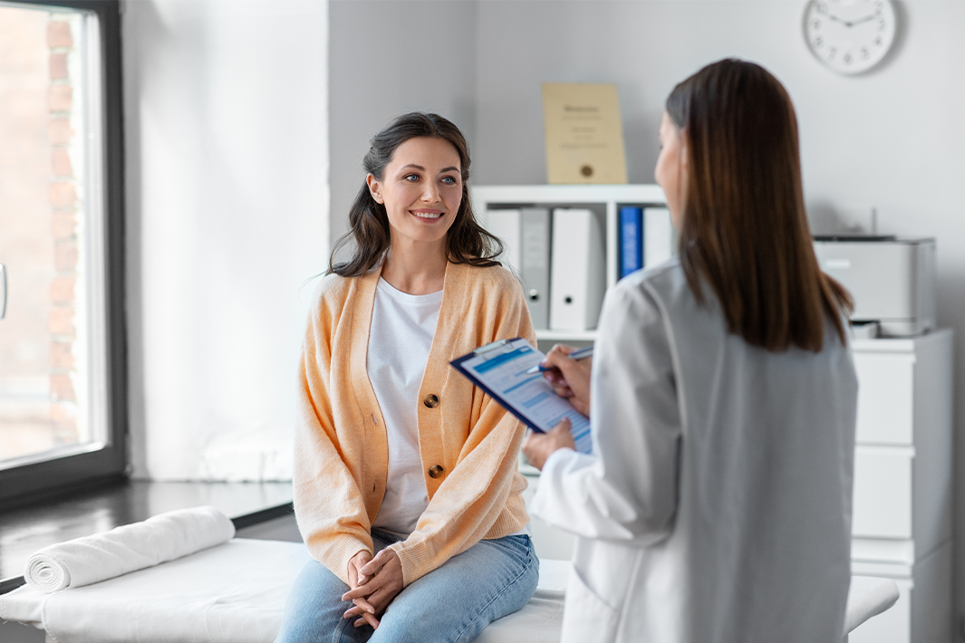 Female doctor with clipboard talking to smiling female patient at hospital.