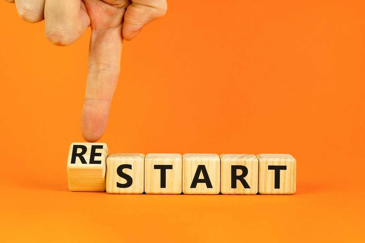 Finger flipping a wooden block from "RE" to "START" on an orange background.