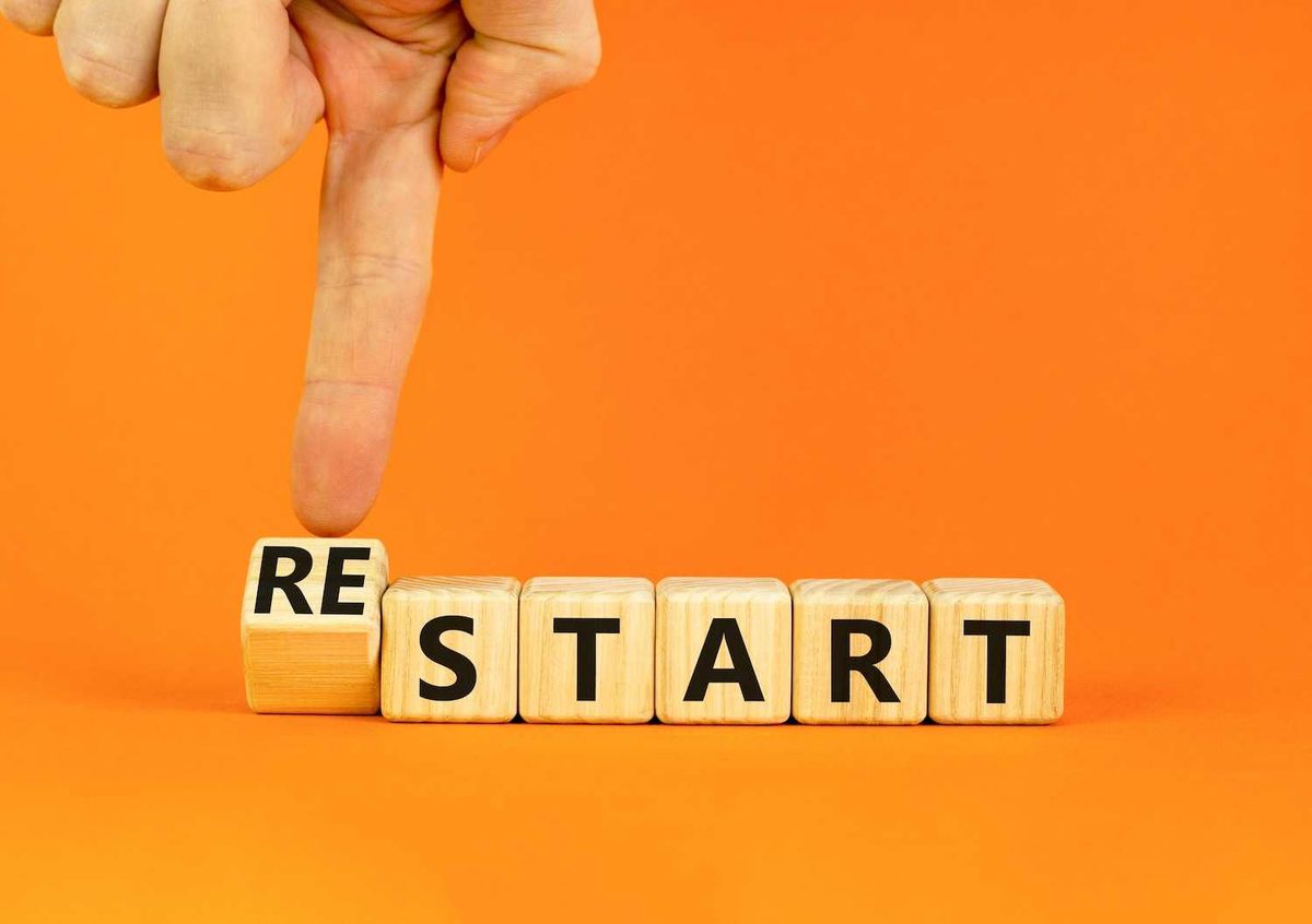 Finger pushing block to form "RESTART" on orange background.