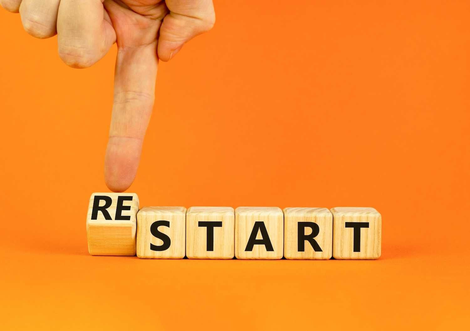 Finger pushing block to form "restart" on orange background.