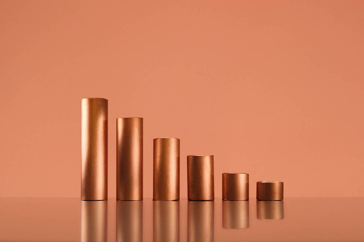Five bronze cylinders of varying heights stand on a reflective surface against an orange background.