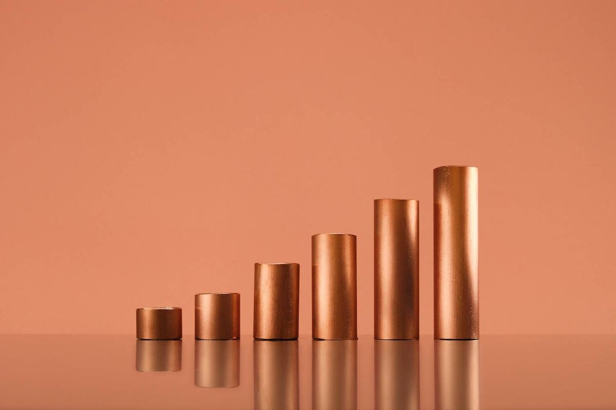 Five copper cylinders arranged by increasing height on a reflective surface.
