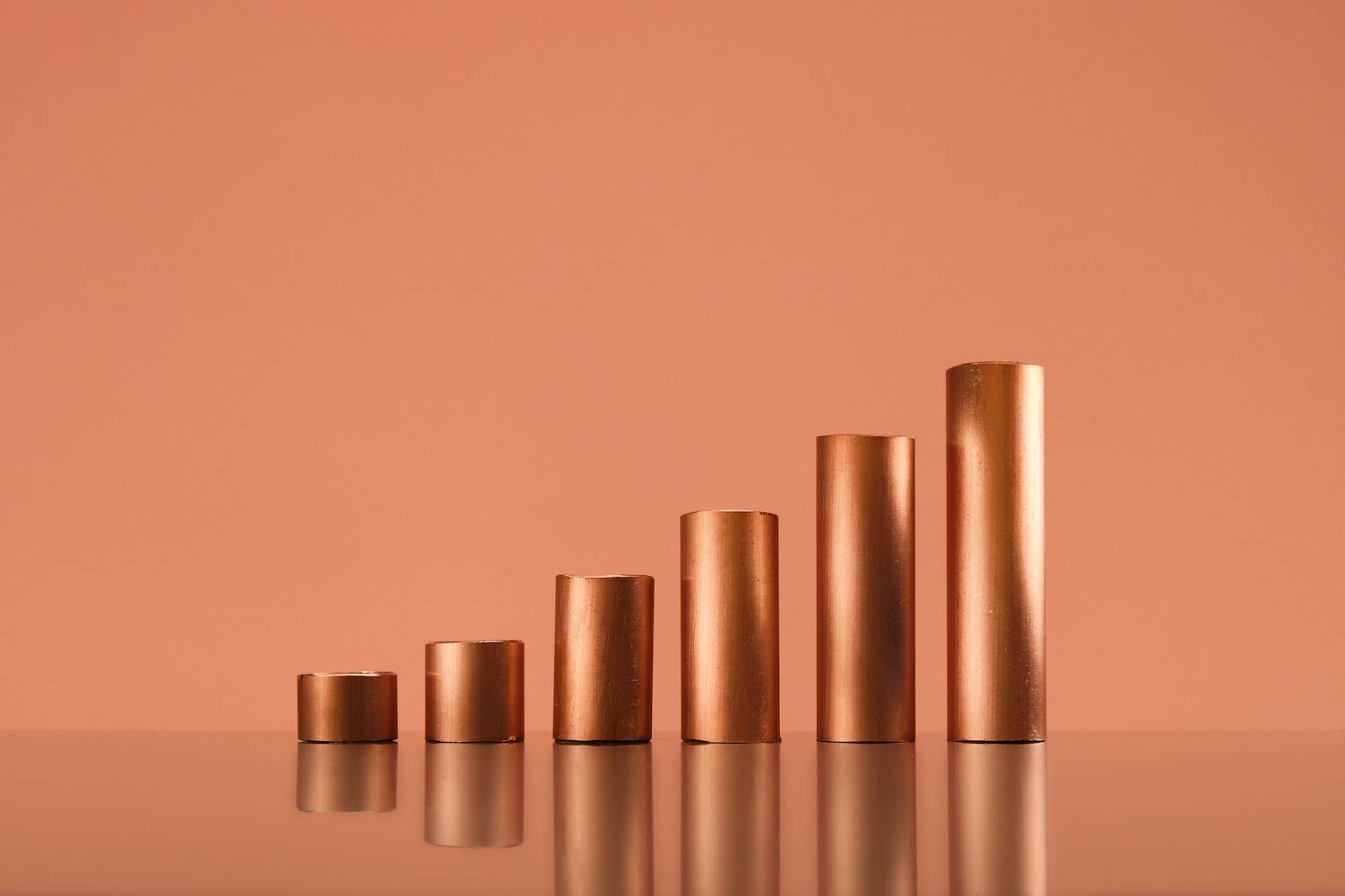 Five copper cylinders increasing in height on a reflective surface.