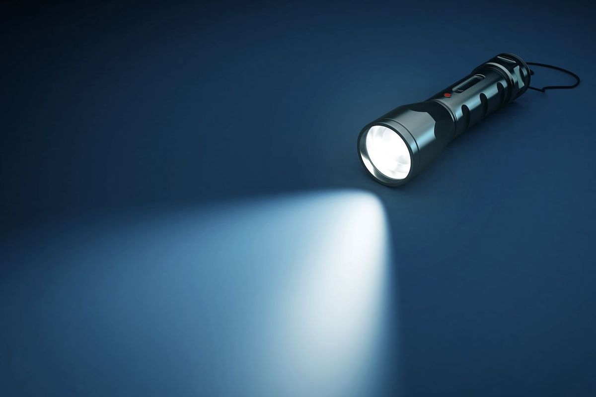 Flashlight casting a beam of light on a dark blue surface.