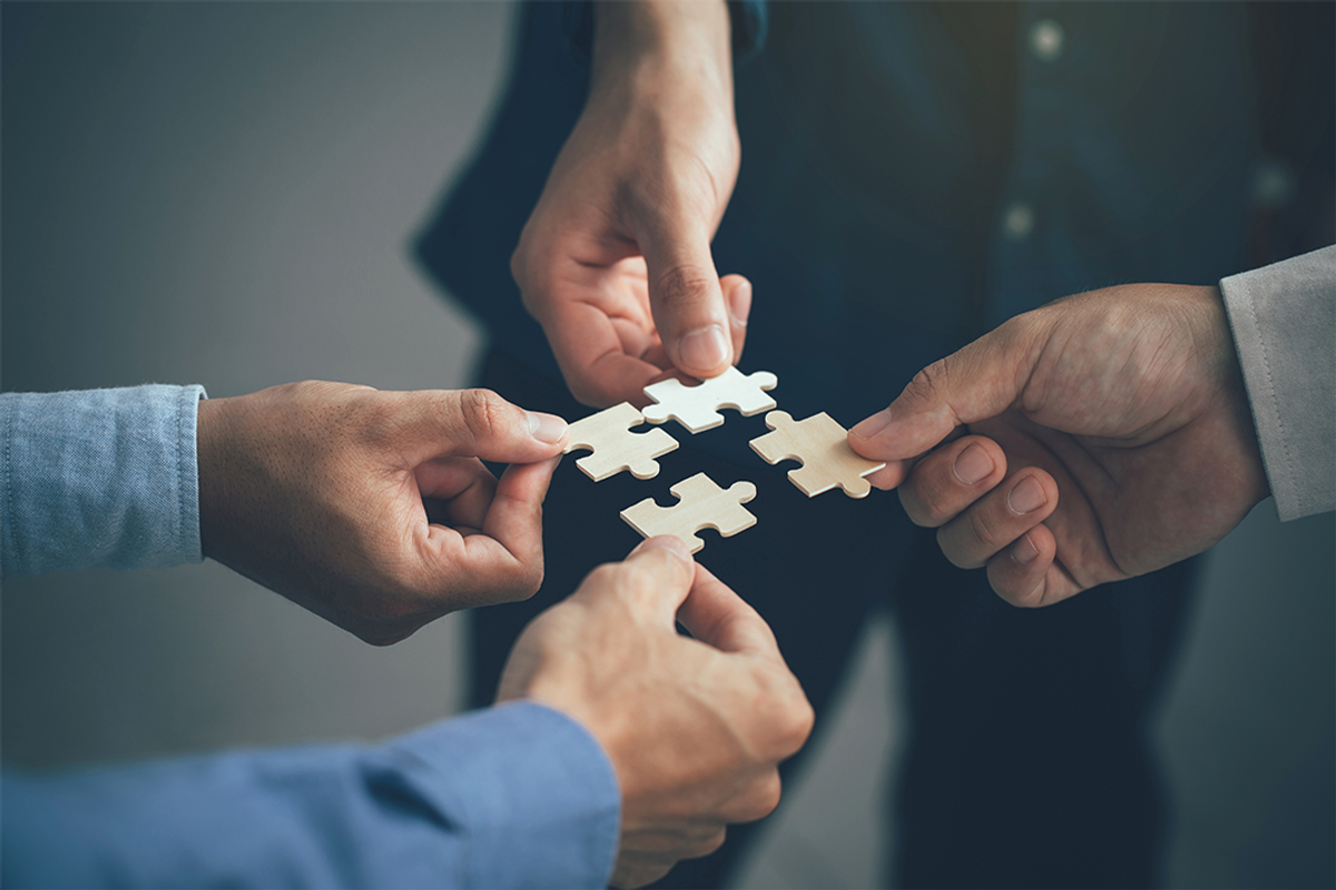 Four hands holding puzzle pieces together.